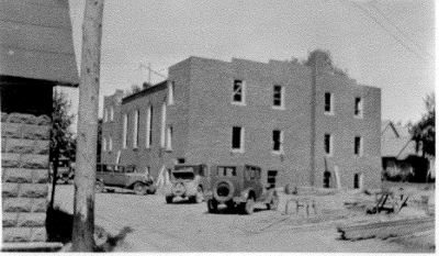 Construction vehicles in front of a partially completed brick church.